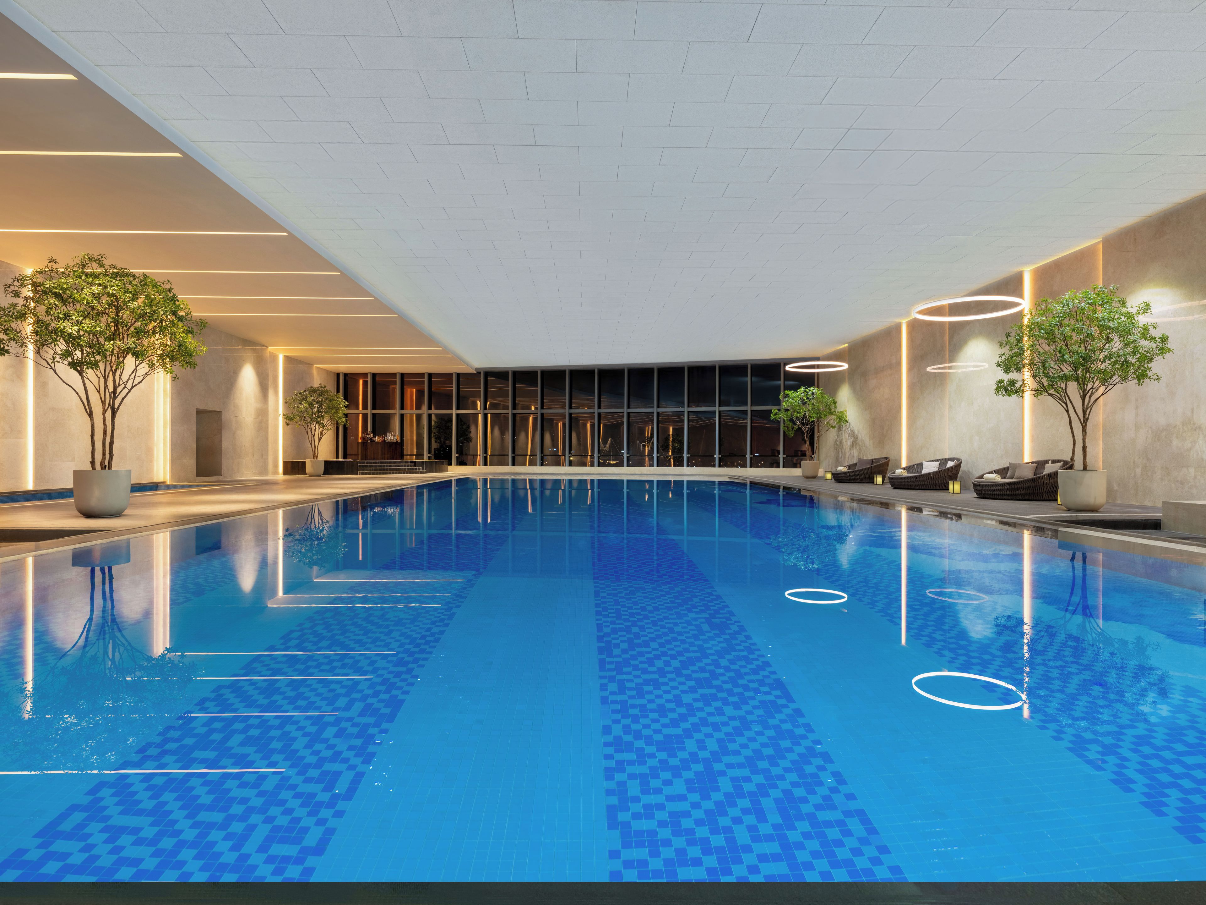 An indoor swimming pool with clear blue water, surrounded by lounge chairs and potted plants.