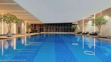 An indoor swimming pool with clear blue water, surrounded by lounge chairs and potted plants.