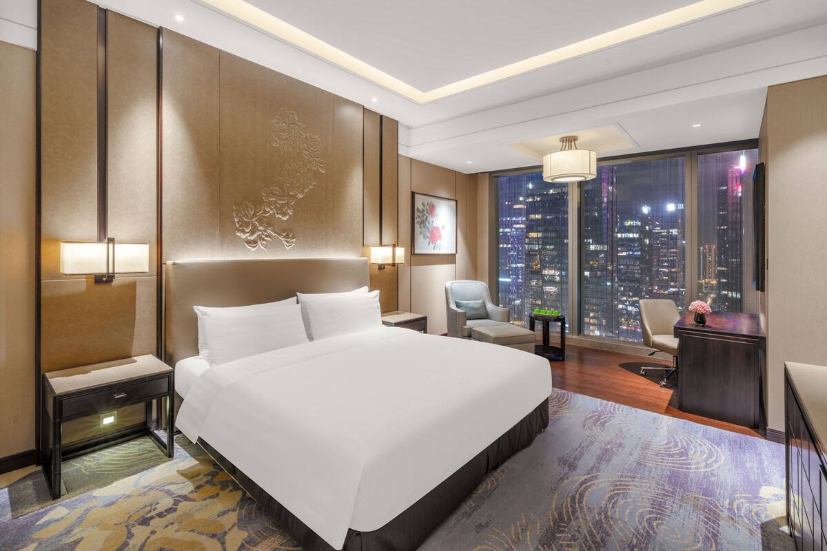 Una habitación de hotel moderna con una cama grande, un escritorio, una silla y vistas de la ciudad.
