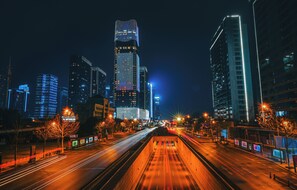 Un paisaje urbano nocturno con rascacielos iluminados y una calle concurrida que muestra estelas de luz.