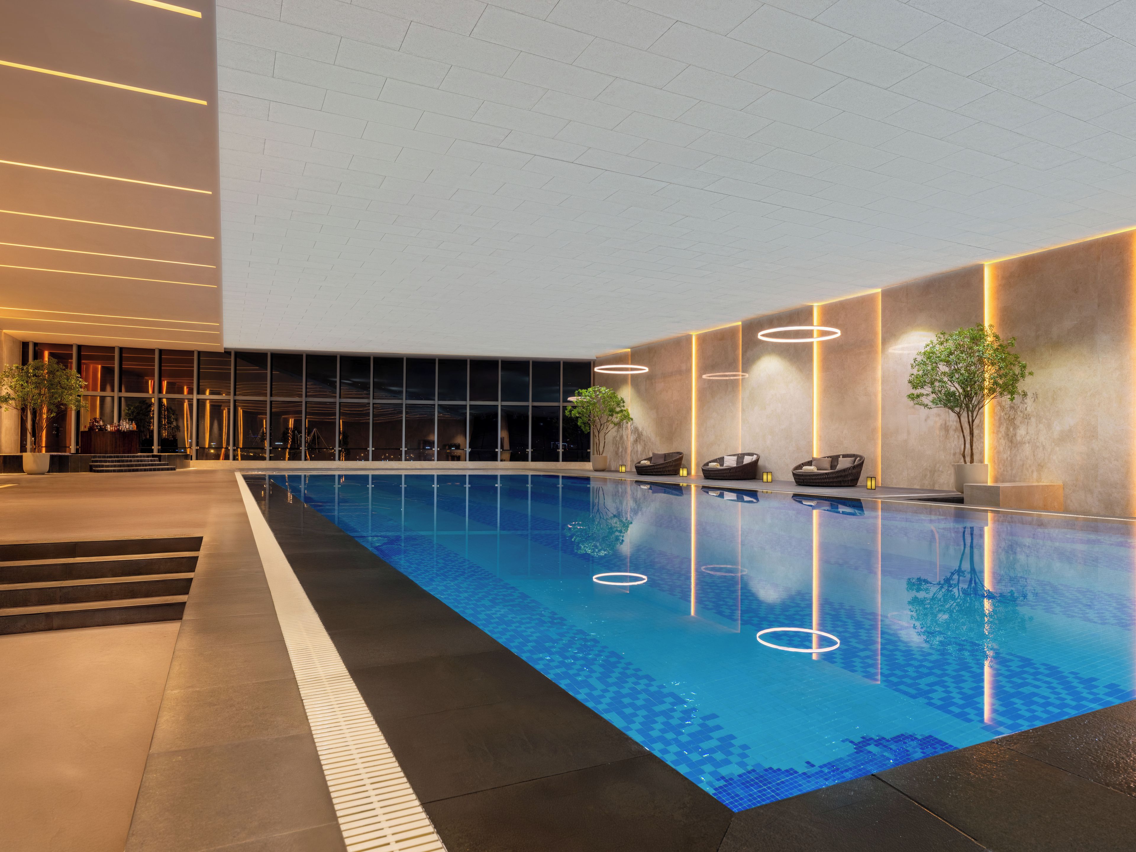 Piscina interna com superfície de água azul translúcida, rodeada por um design moderno com padrões geométricos no chão e iluminada por iluminação embutida.