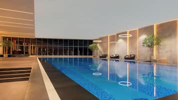 Piscina interna com superfície de água azul translúcida, rodeada por um design moderno com padrões geométricos no chão e iluminada por iluminação embutida.