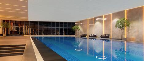 Ein Innenpool mit klarer, blauer Wasseroberfläche, umgeben von modernem Design mit geometrischen Mustern auf dem Boden und beleuchtet durch eingelassene Spots.