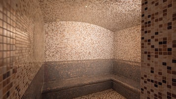 A room with a mosaic-tiled wall and floor, a curved bench, and a ceiling with recessed lighting.