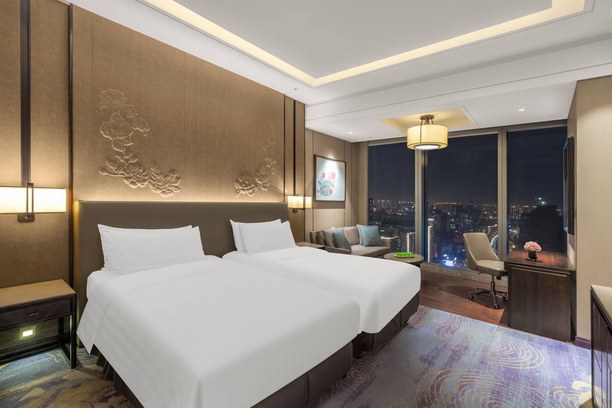 Una habitación de hotel moderna con una cama grande, un sofá, un escritorio y vistas a la ciudad de noche.