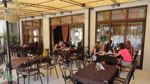 An outdoor cafe with tables and chairs, large windows, and a yellow awning. - Cantilena Complex (Sunny Beach)