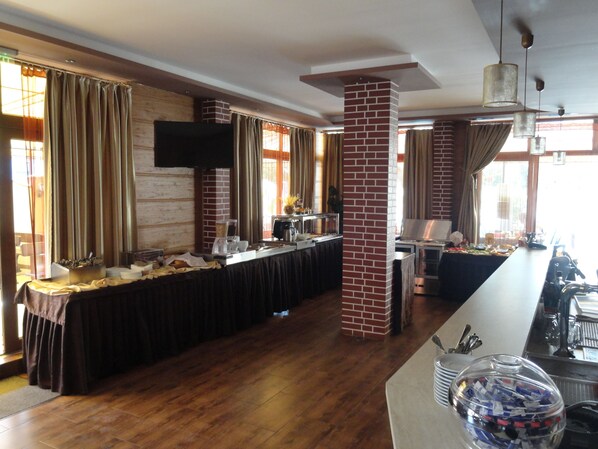 A hotel room with a long dining table, a brick pillar, and a television mounted on the wall.