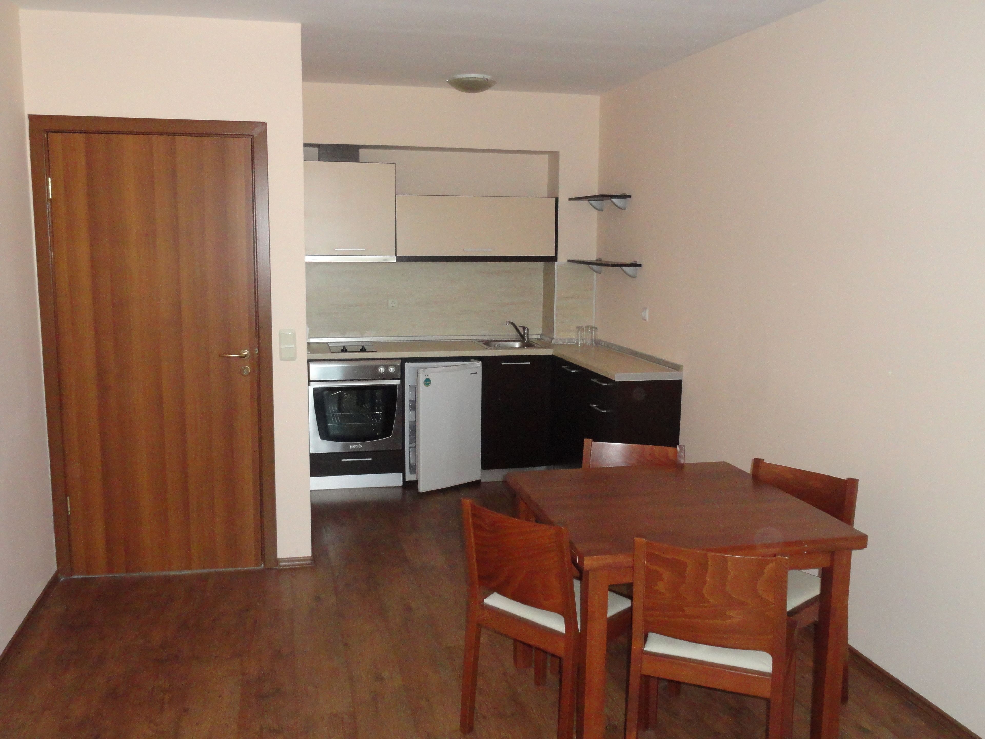 A compact kitchen with a wooden table and chairs, a built-in oven, and a refrigerator.