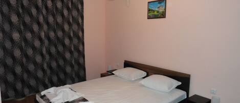 A bedroom with a bed, a nightstand, an air conditioner, a painting, and a patterned curtain.