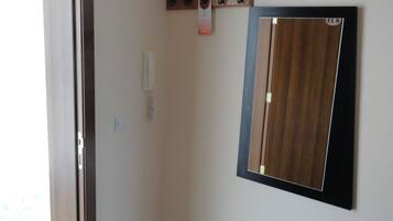A corner room with a door, a wall-mounted mirror, a coat rack, and a light switch.