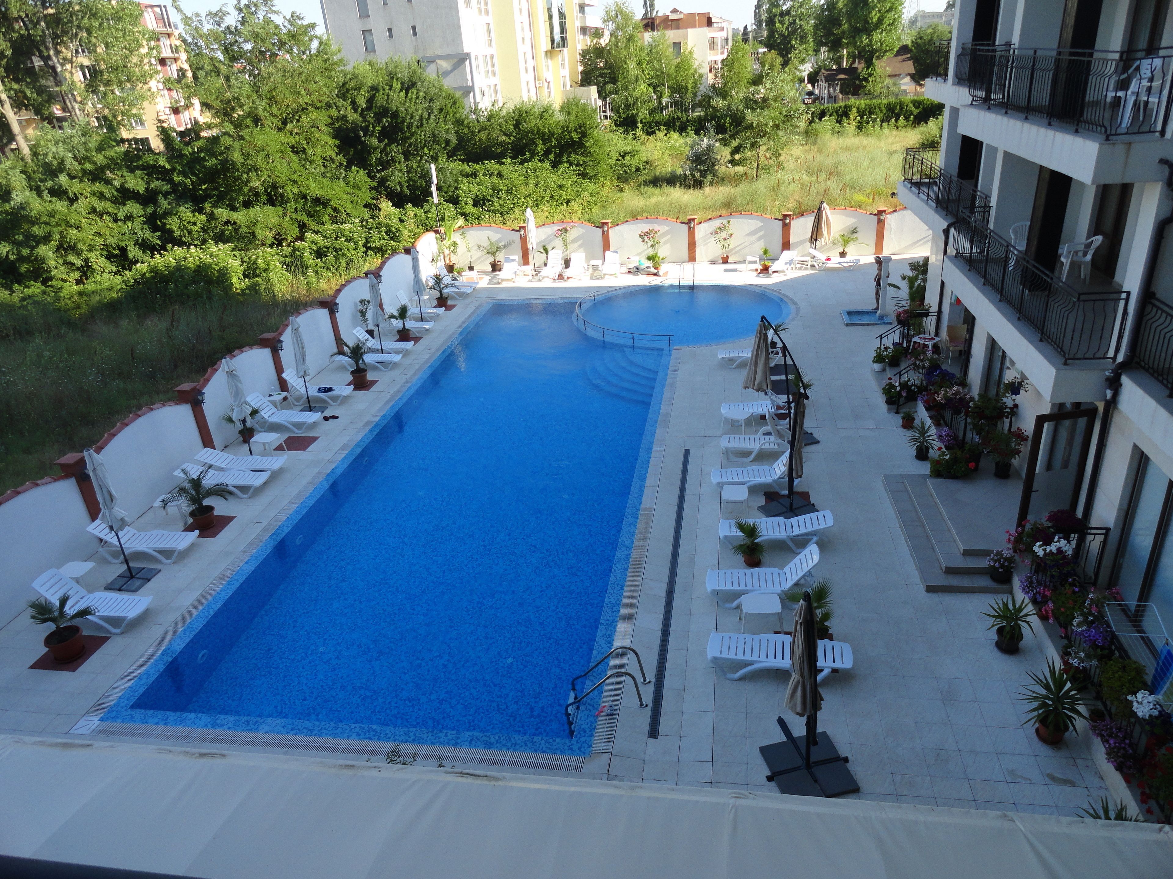A rectangular swimming pool with white lounge chairs and umbrellas arranged around its perimeter.