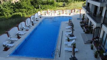 A rectangular swimming pool with white lounge chairs and umbrellas arranged around its perimeter.