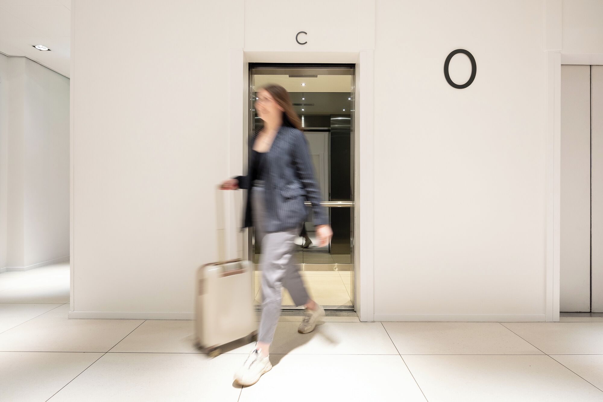 A modern interior with a minimalist design, featuring a prominent 'C' sign above a door, a circular logo on the wall, and a clean, tiled floor.