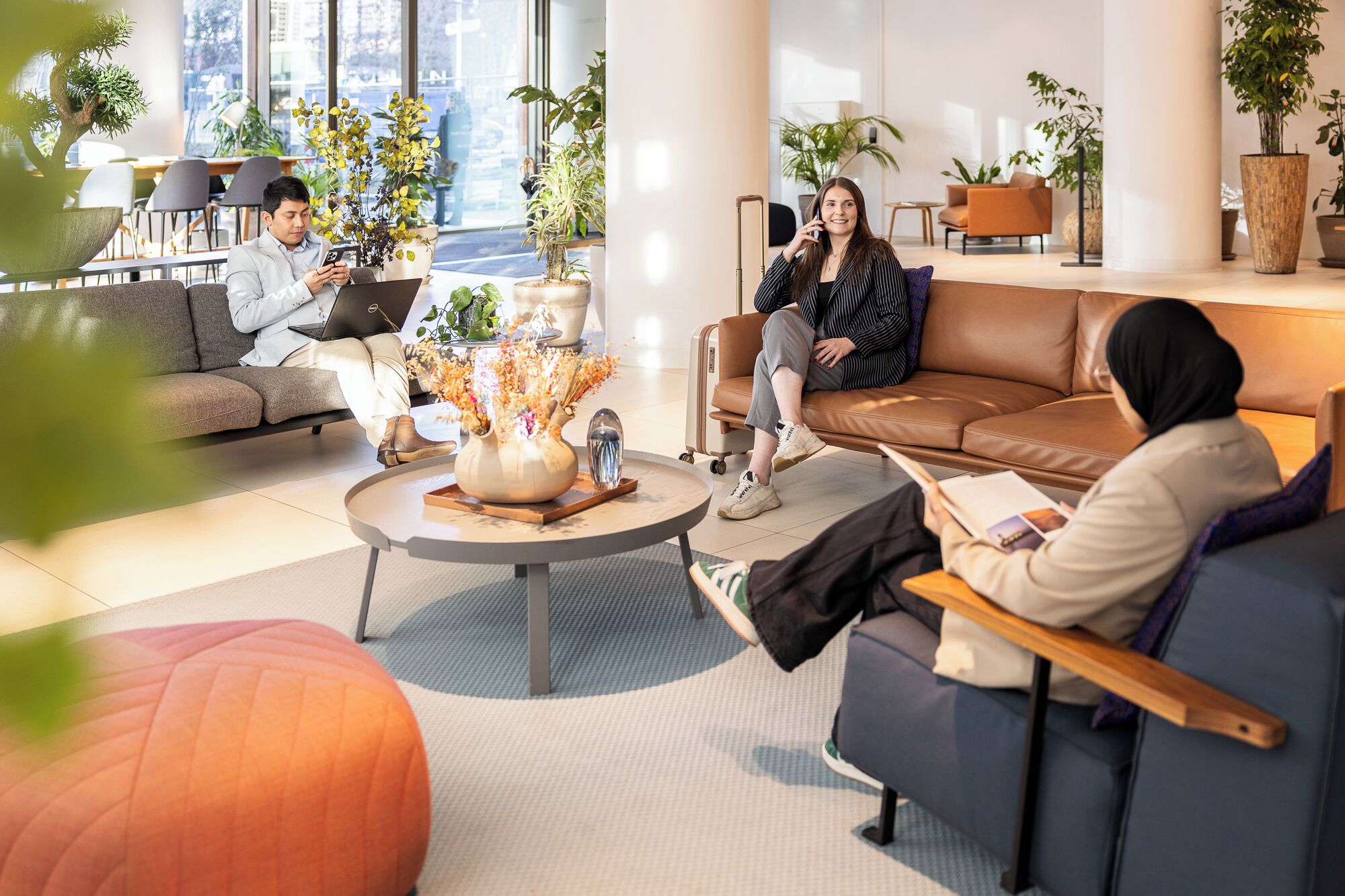 A modern lounge area with leather sofas, a coffee table with a vase, and potted plants.