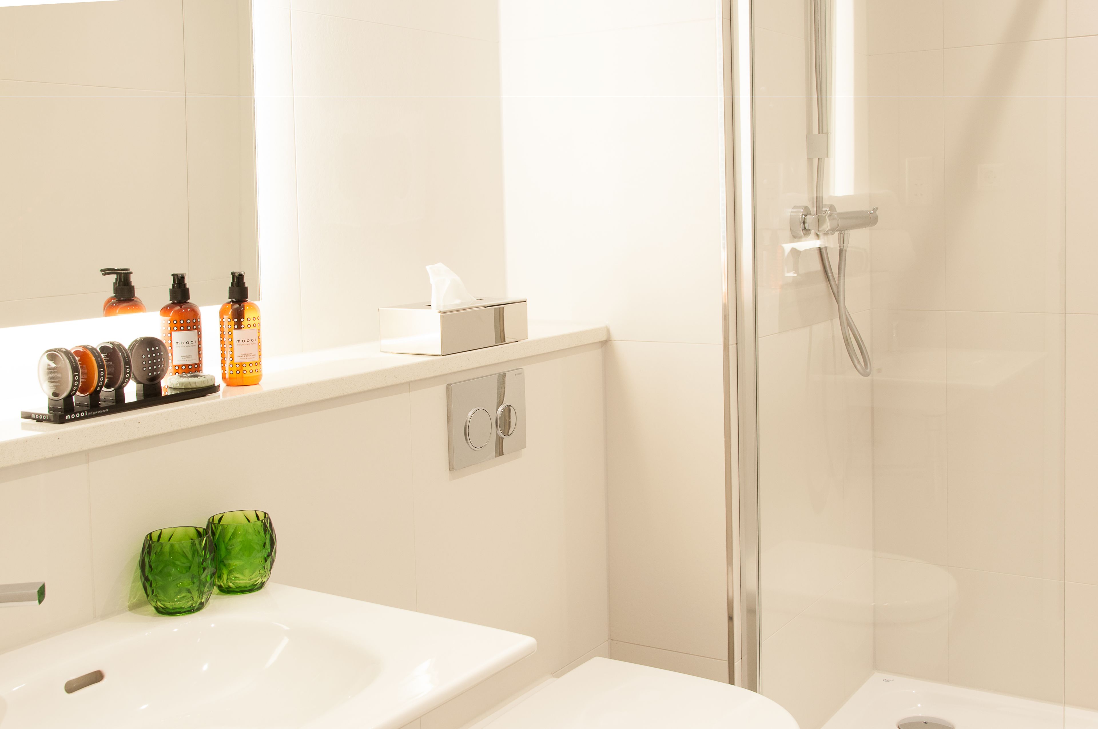 A modern bathroom with a white sink, green glass cups, and toiletries on the counter.