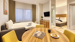 Ett modernt hotellrum med en säng, en soffa, ett matbord och en TV.