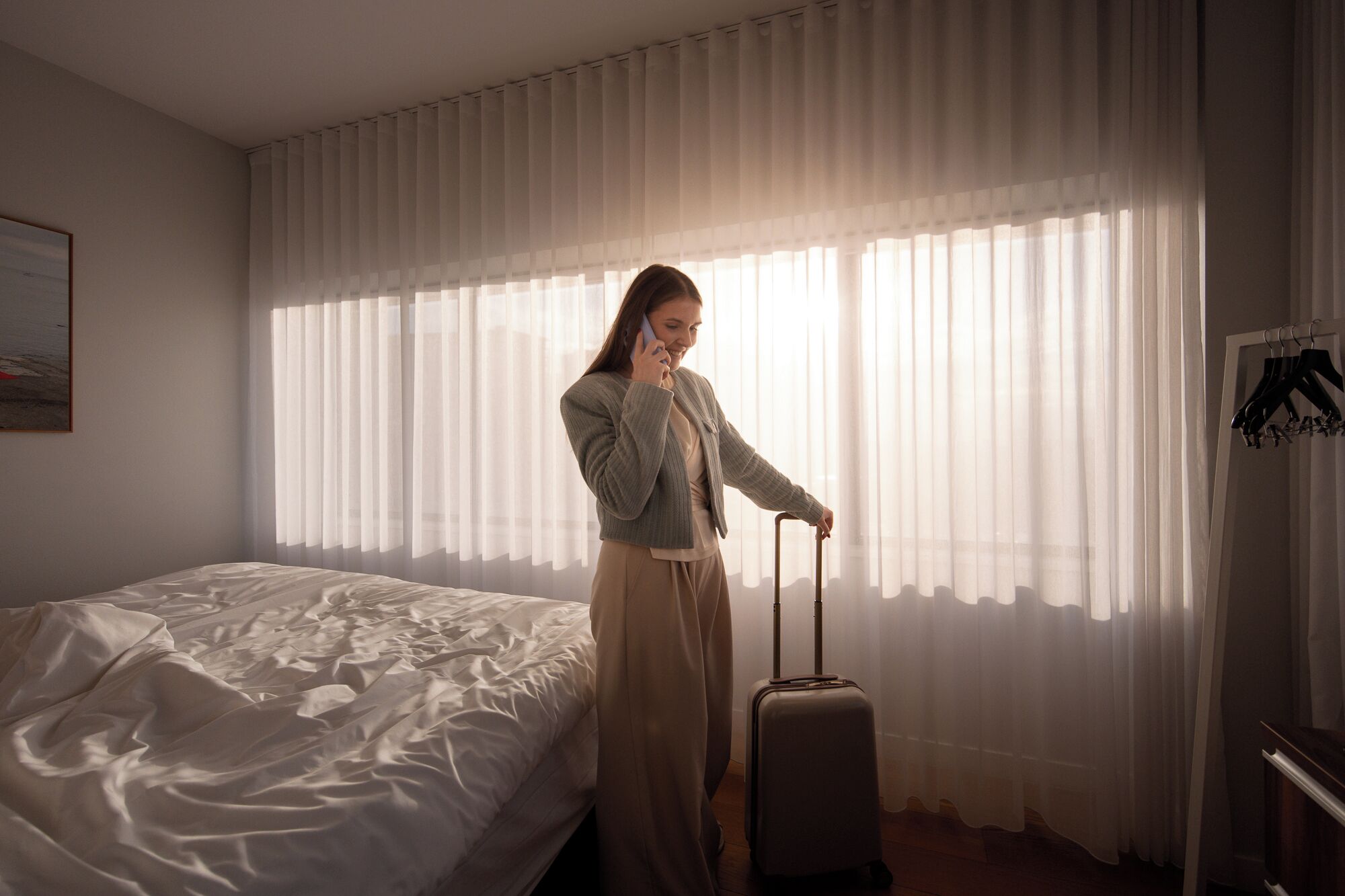 A hotel room with a bed, a suitcase, and a coat rack with hangers.