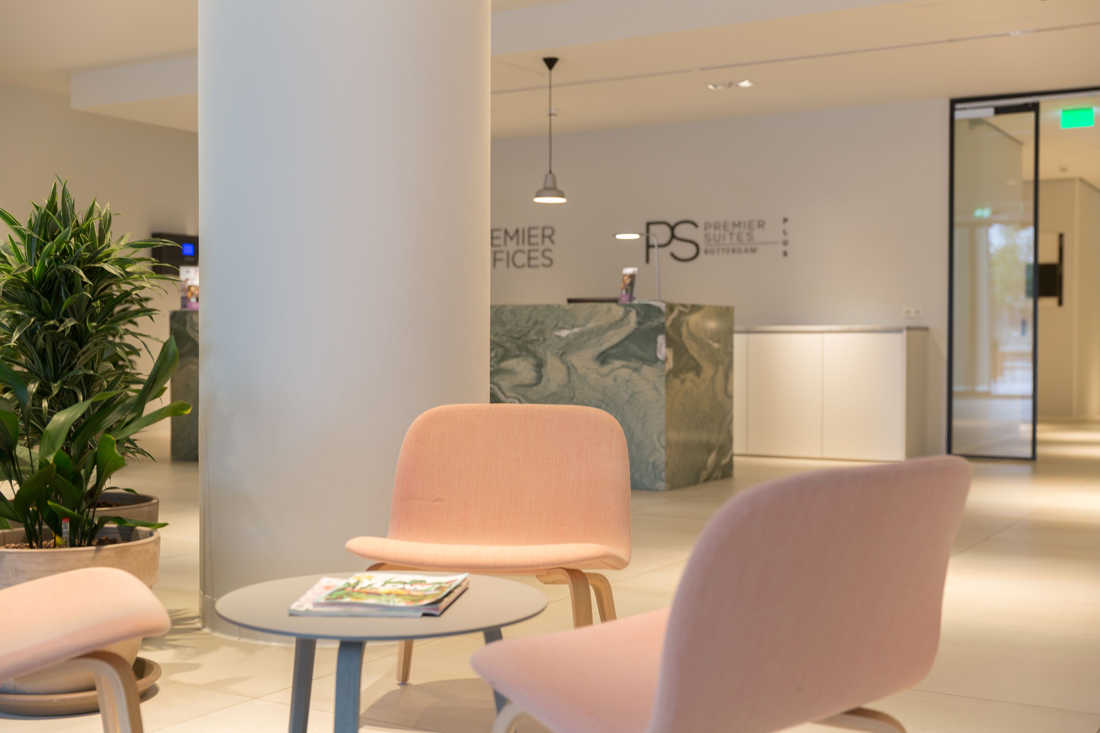 Un hall d’entrée moderne avec un comptoir d’accueil, une plante en pot et deux fauteuils roses disposés autour d’une petite table.