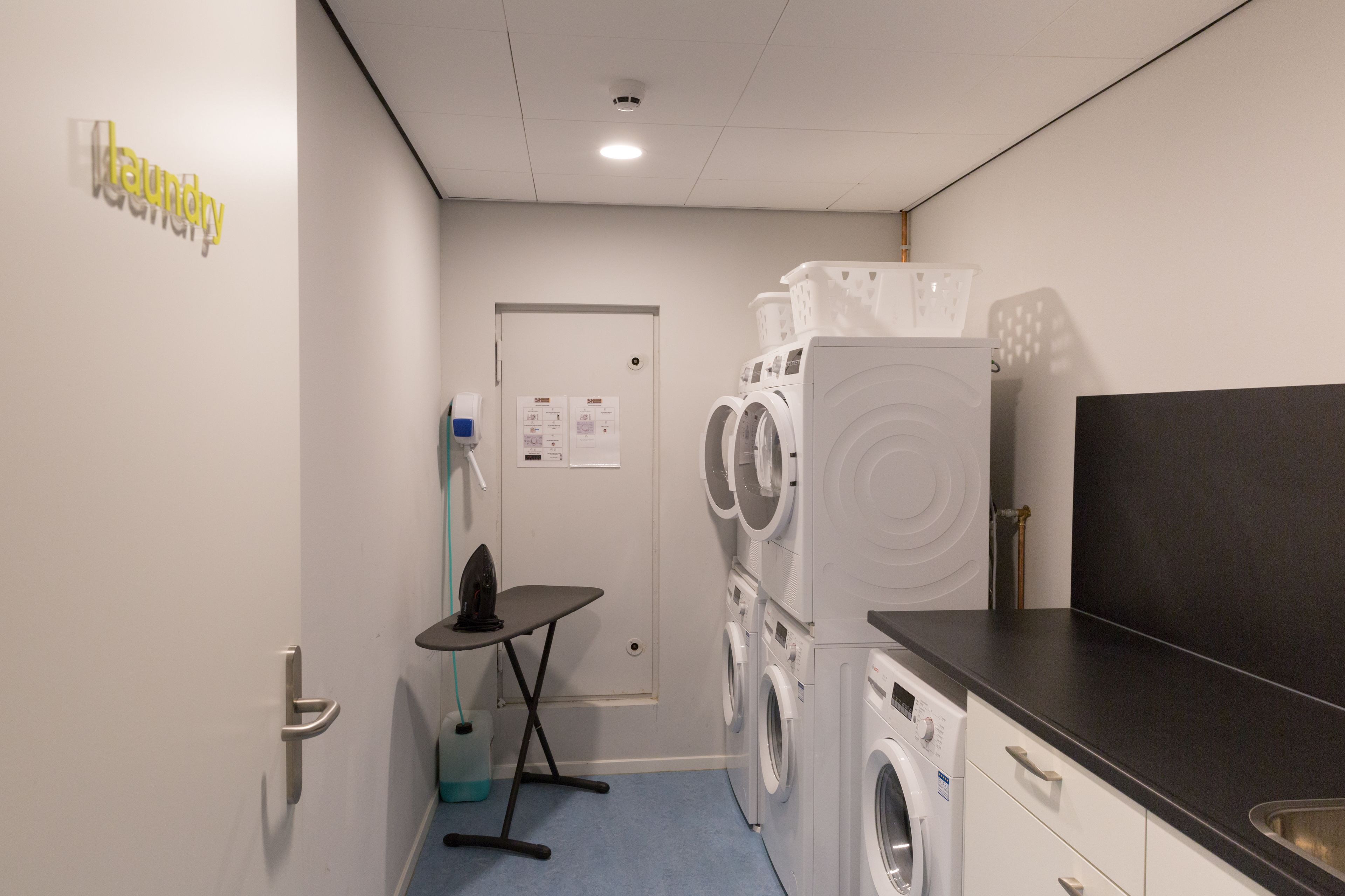Une buanderie équipée d’un lave-linge, d’un sèche-linge, d’une planche à repasser et d’un évier.