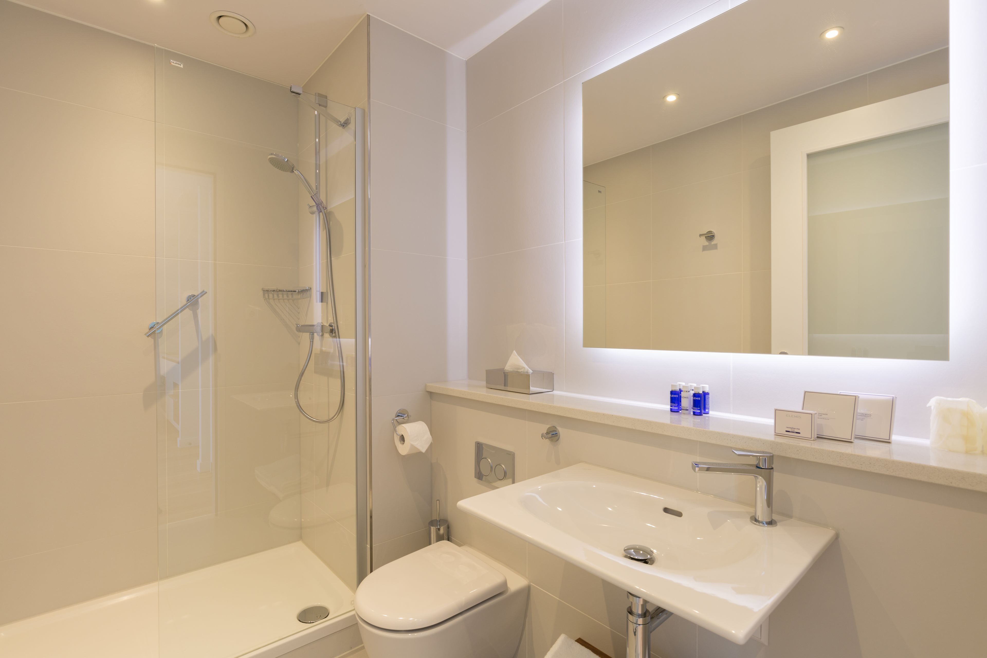 Et moderne badeværelse med brusebad bag glas, en hvid vask og et toilet.