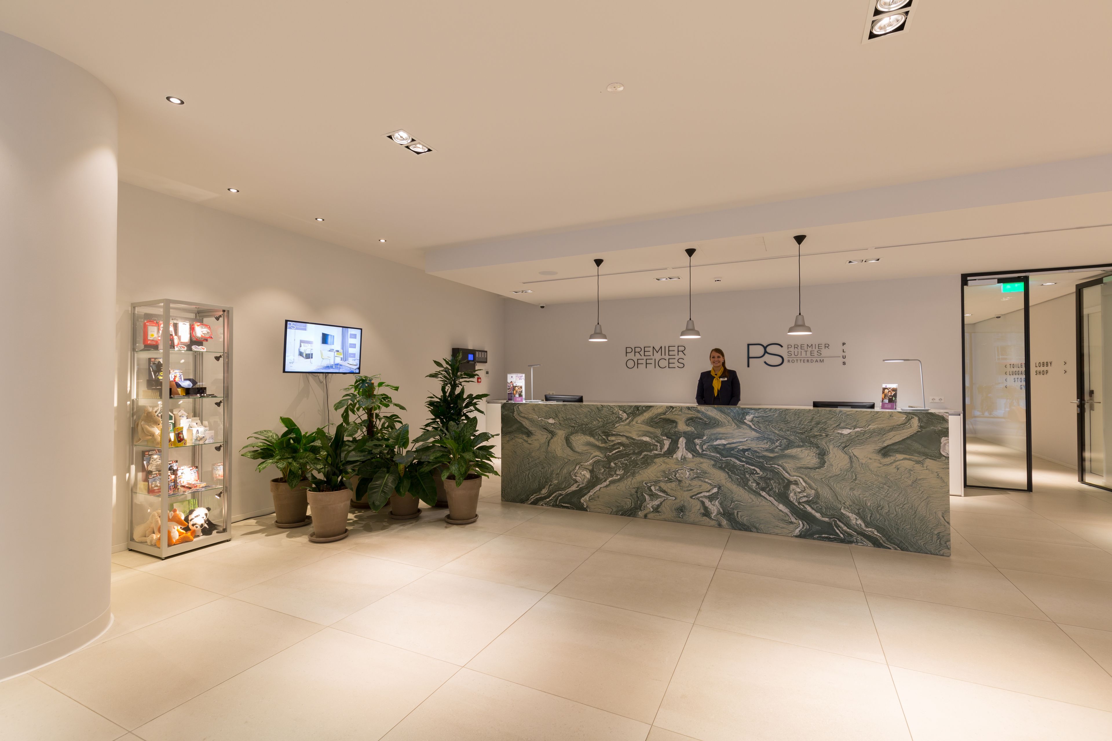 Un hall d’accueil moderne, avec un comptoir en marbre, des plantes en pot, un téléviseur et un panneau indiquant « Premier Suites ».