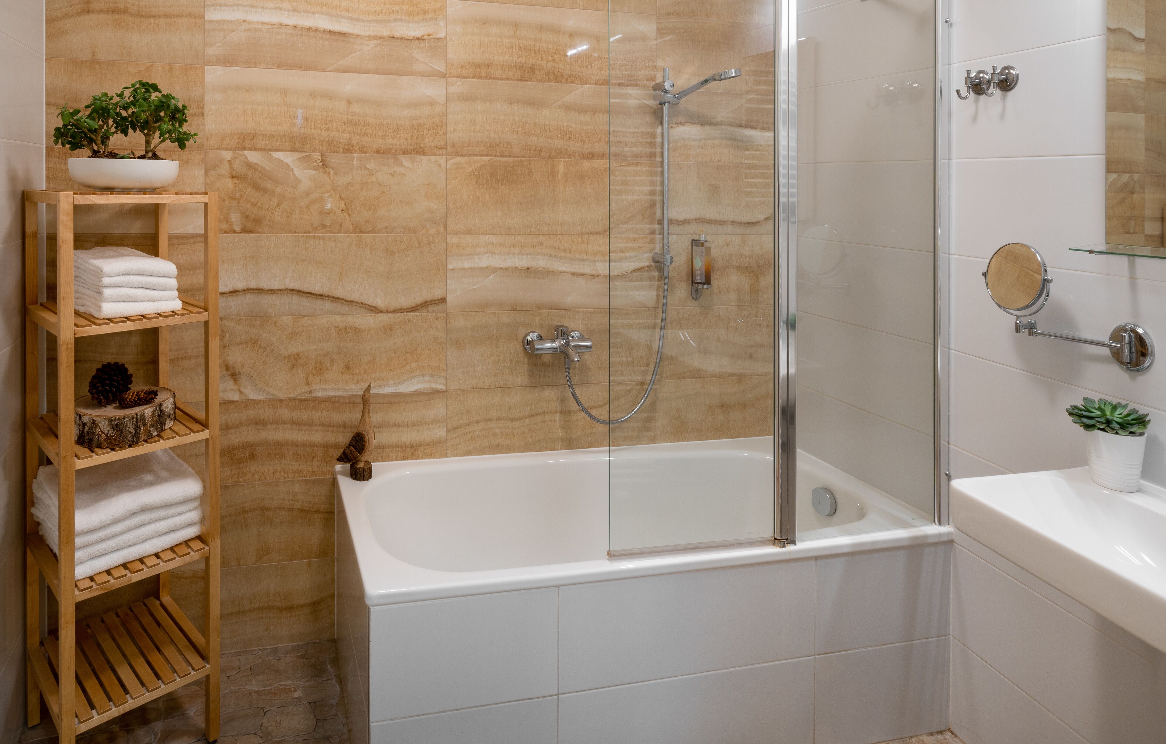 A modern bathroom with a glass-enclosed shower, a white bathtub, and a wooden shelf with towels and a potted plant.