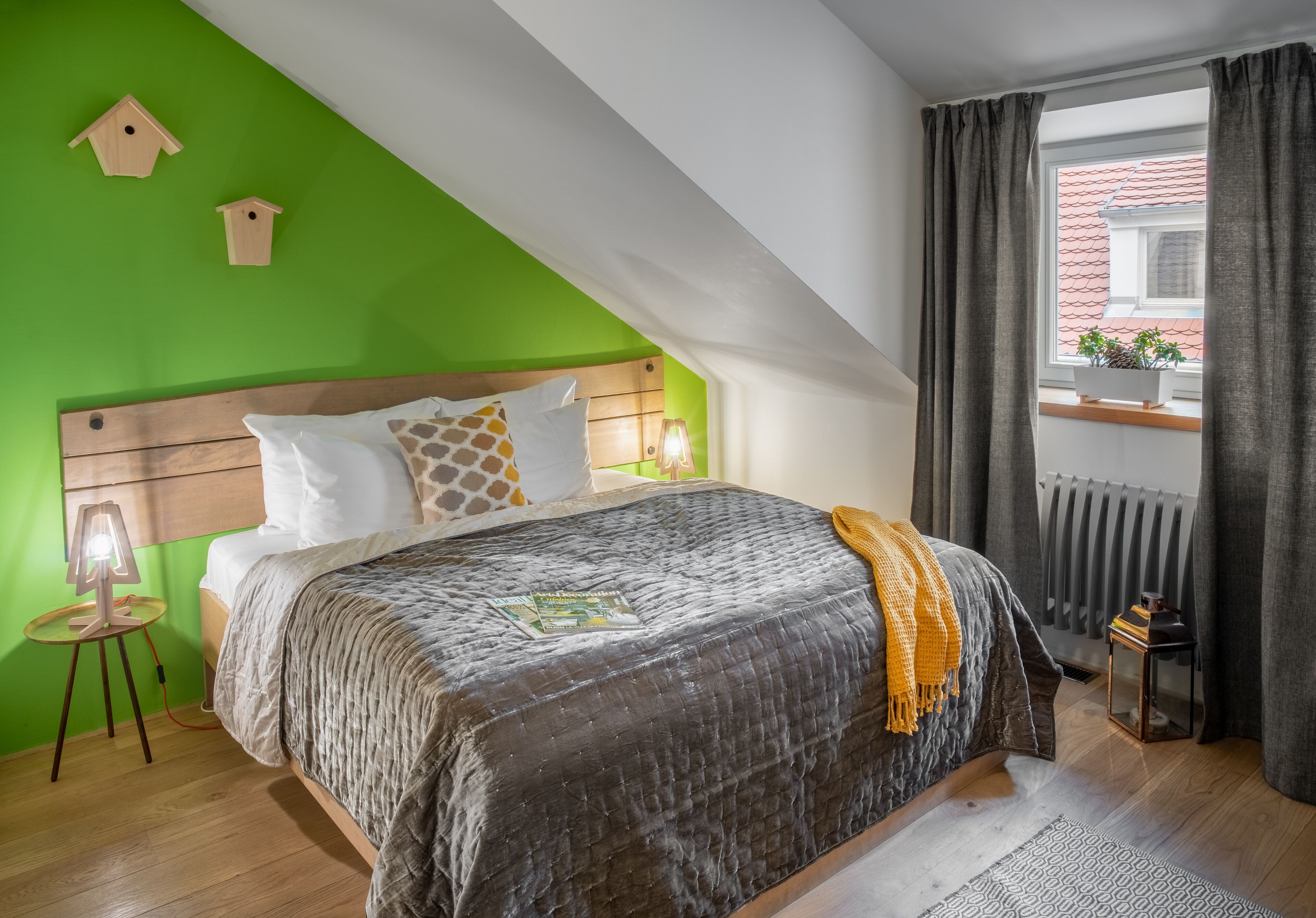 A bedroom with a sloped ceiling, a bed with a quilted cover, a wooden headboard, and a window with curtains.