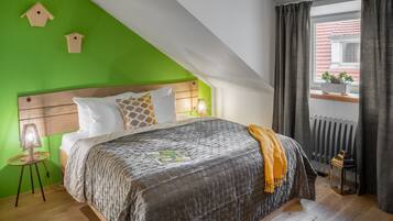 A bedroom with a sloped ceiling, a bed with a quilted cover, a wooden headboard, and a window with curtains.