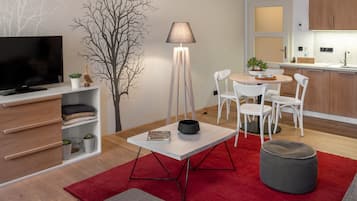 Una sala de estar moderna con televisor de pantalla plana, una lámpara de pie, una mesa de comedor con sillas, una alfombra roja y un otomano gris.