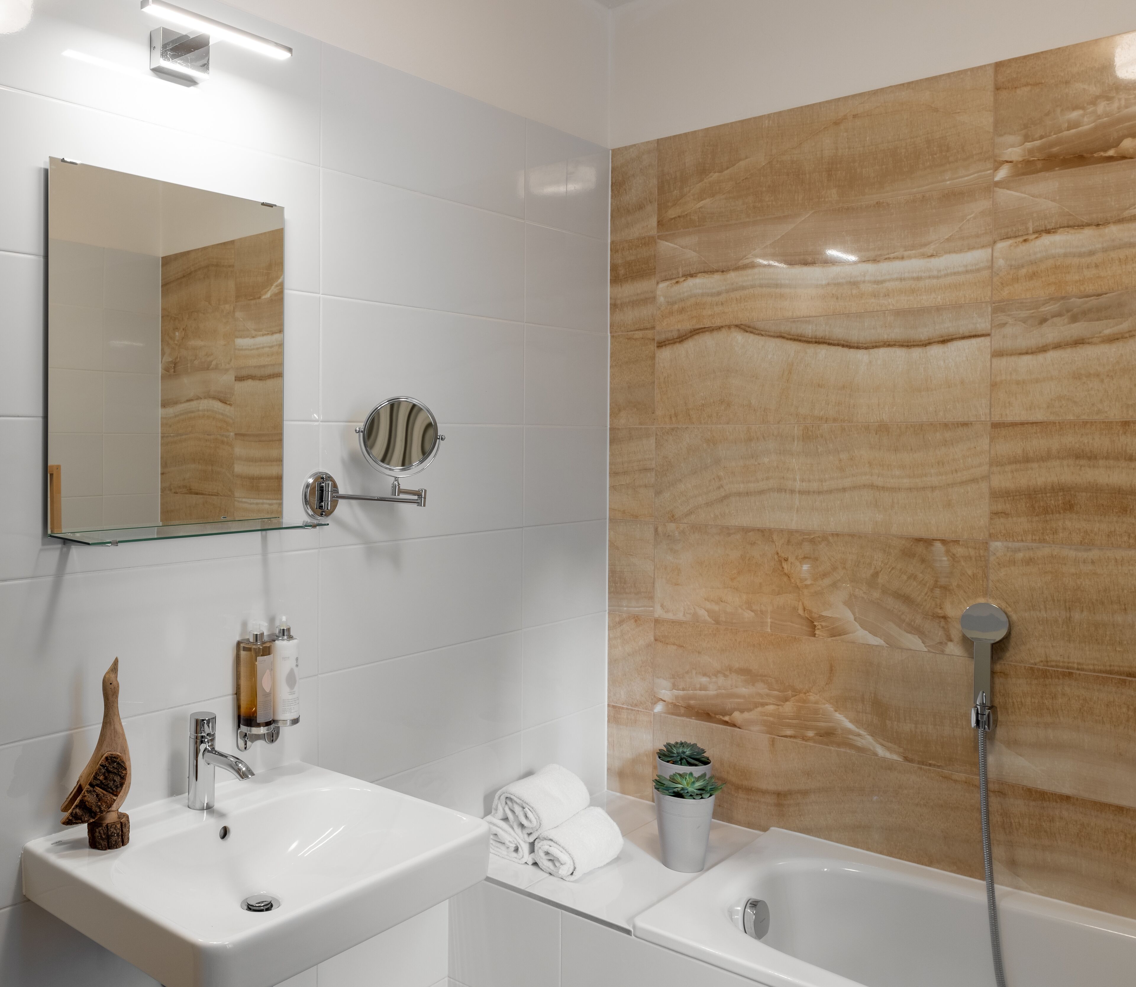 Une salle de bain moderne avec un lavabo blanc, un miroir et une douche dont le mur est recouvert de marbre.