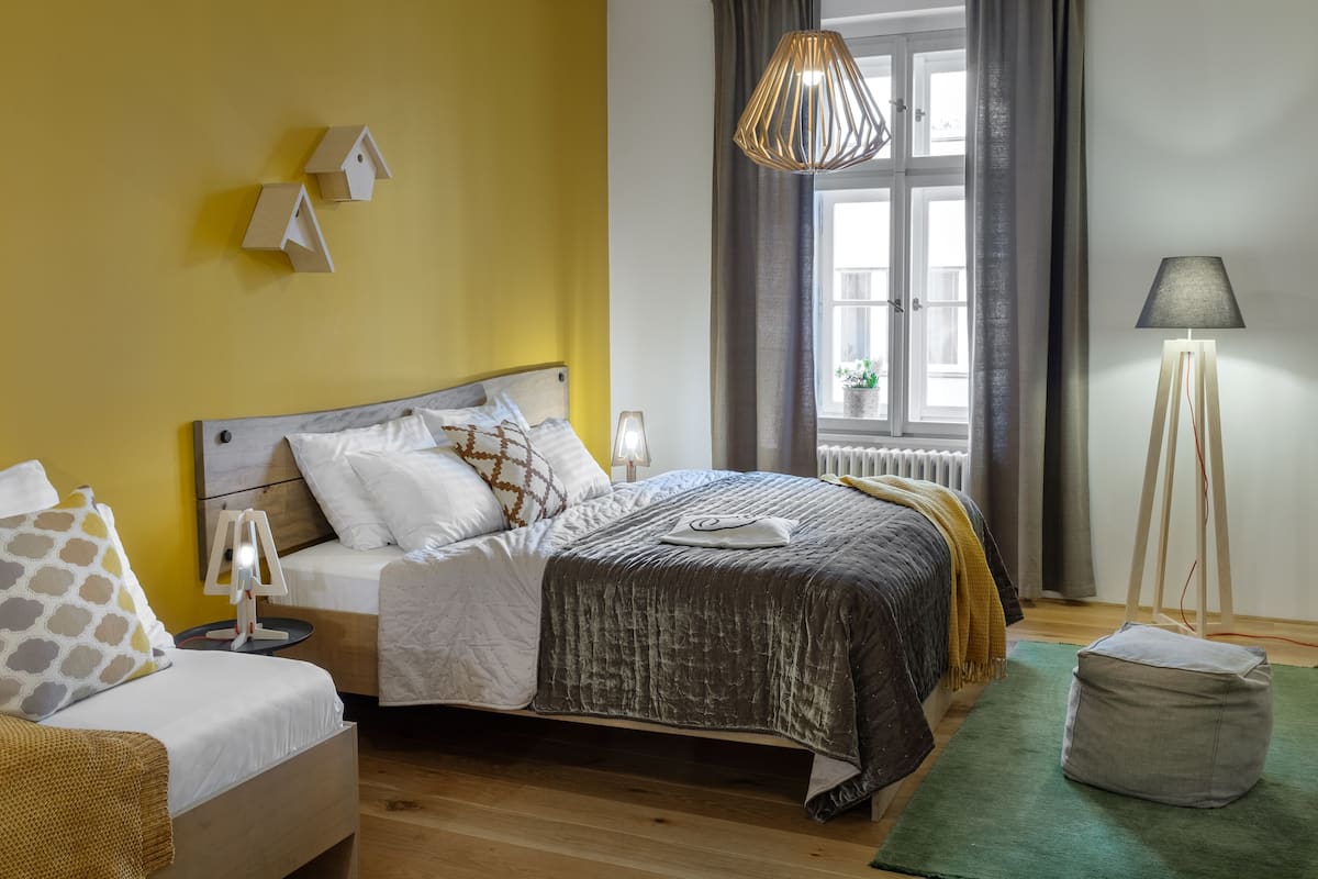 Quarto com cama, mesas de cabeceira, luminária, janela com cortinas e vista para o exterior.