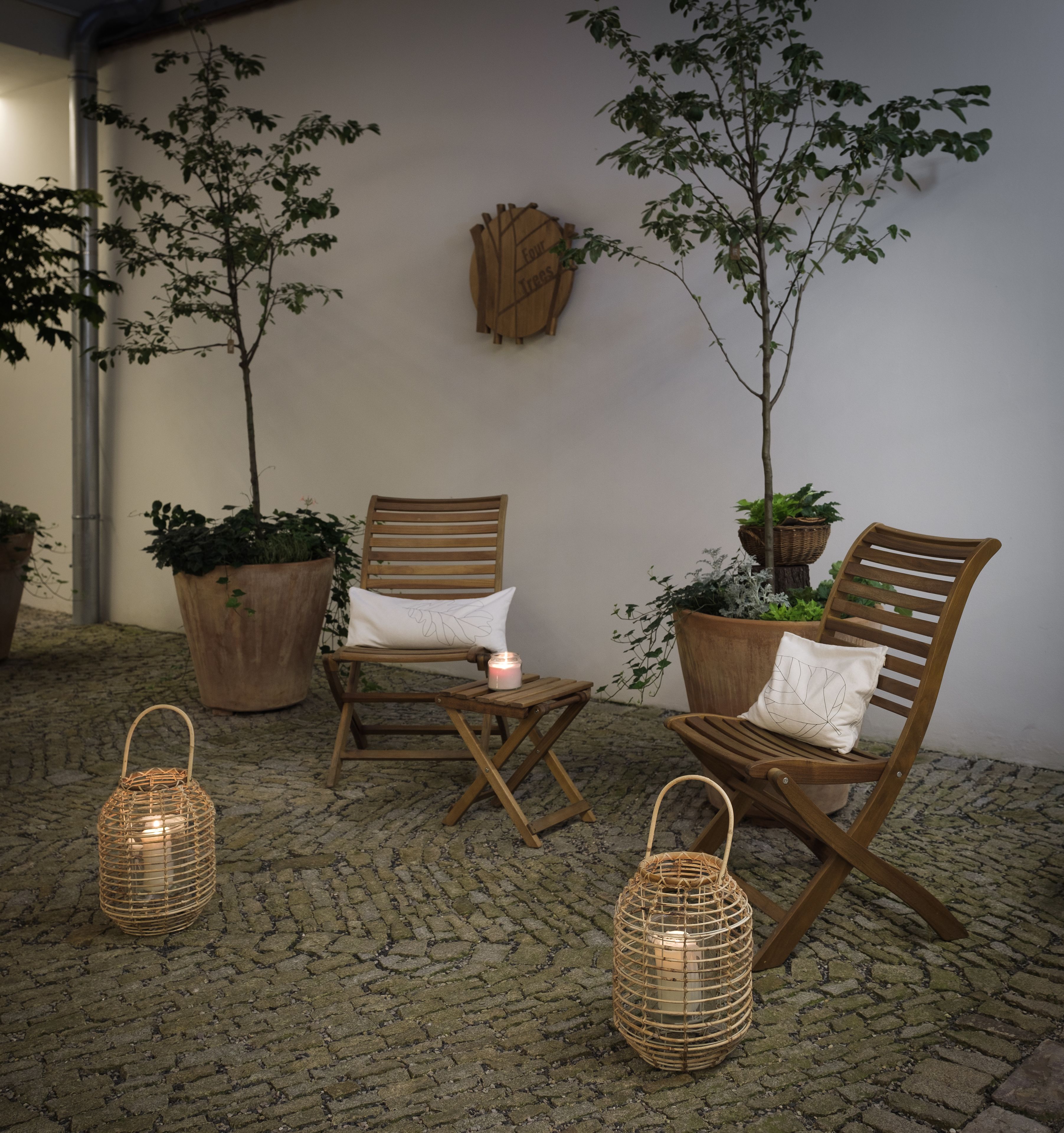 A cozy outdoor seating area with two wooden chairs, a small table, and two wicker lanterns.