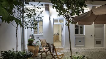Un cortile con un tavolo e sedie in legno, circondato da grandi piante in vaso e un albero.
