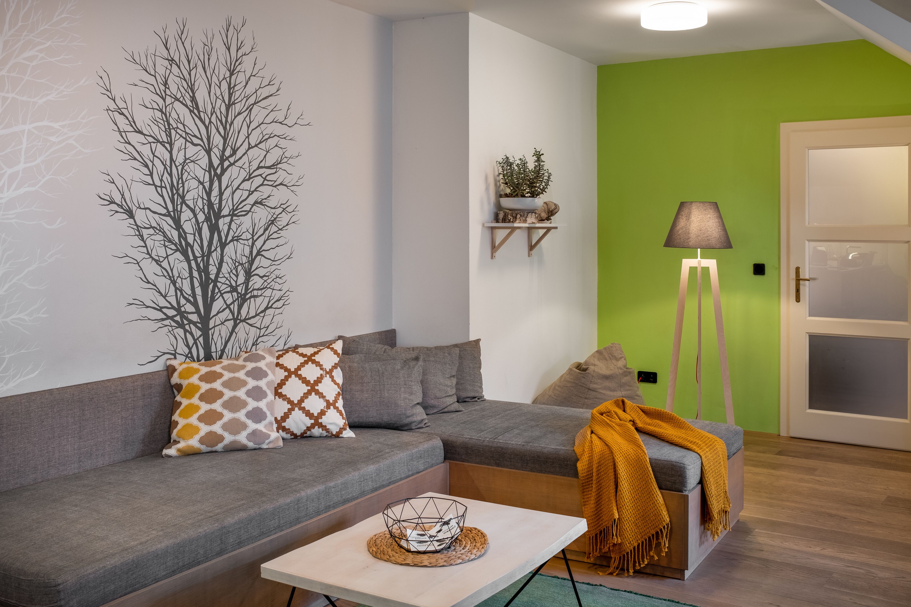 Un soggiorno moderno con un divano grigio, un tavolino bianco e una parete verde decorativa.