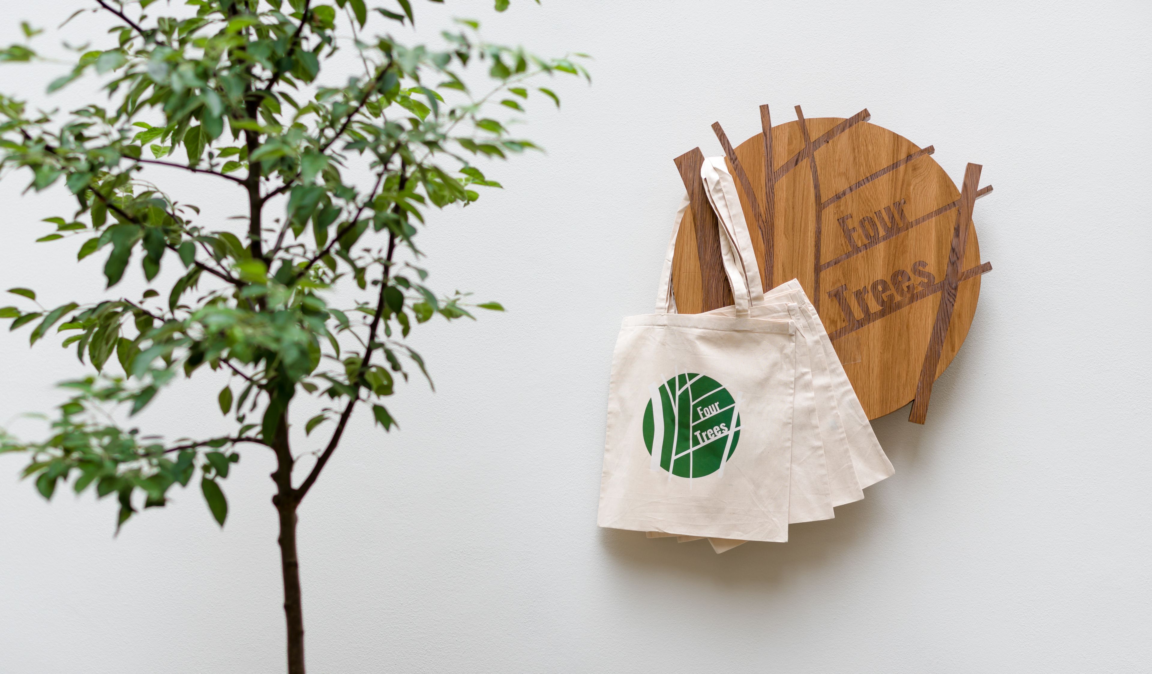 Uma placa de madeira com a inscrição 'full trees', uma sacola de tecido branca com um logotipo verde e um galho de árvore.