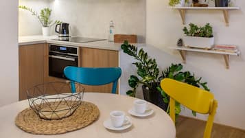 A modern kitchen with wooden cabinets, a built-in oven, a coffee maker, and a dining area with a round table, two chairs, and a woven placemat.