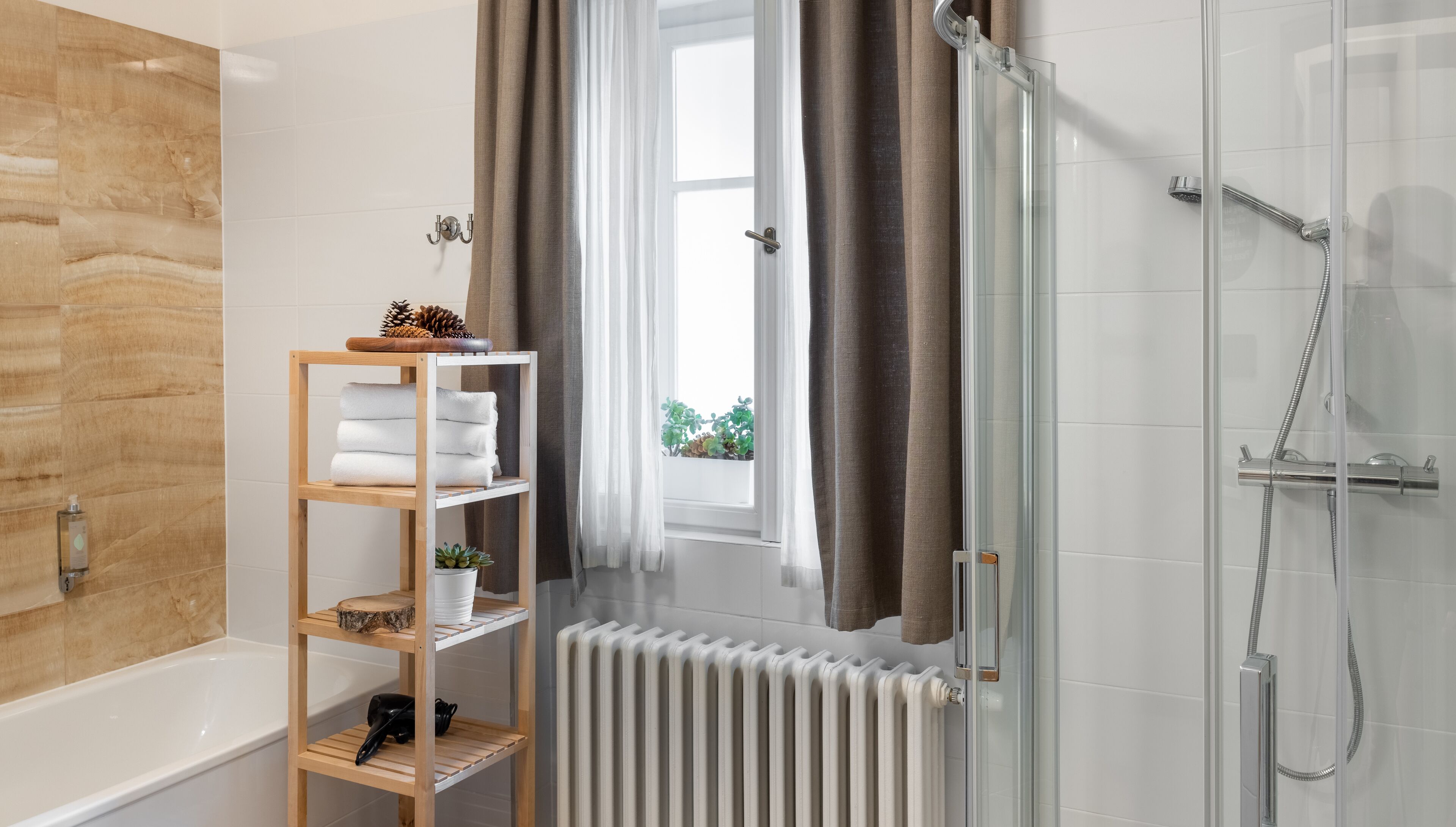 Een moderne badkamer met een glazen douchecabine, een houten plank met handdoeken en uitzicht op groen buiten.