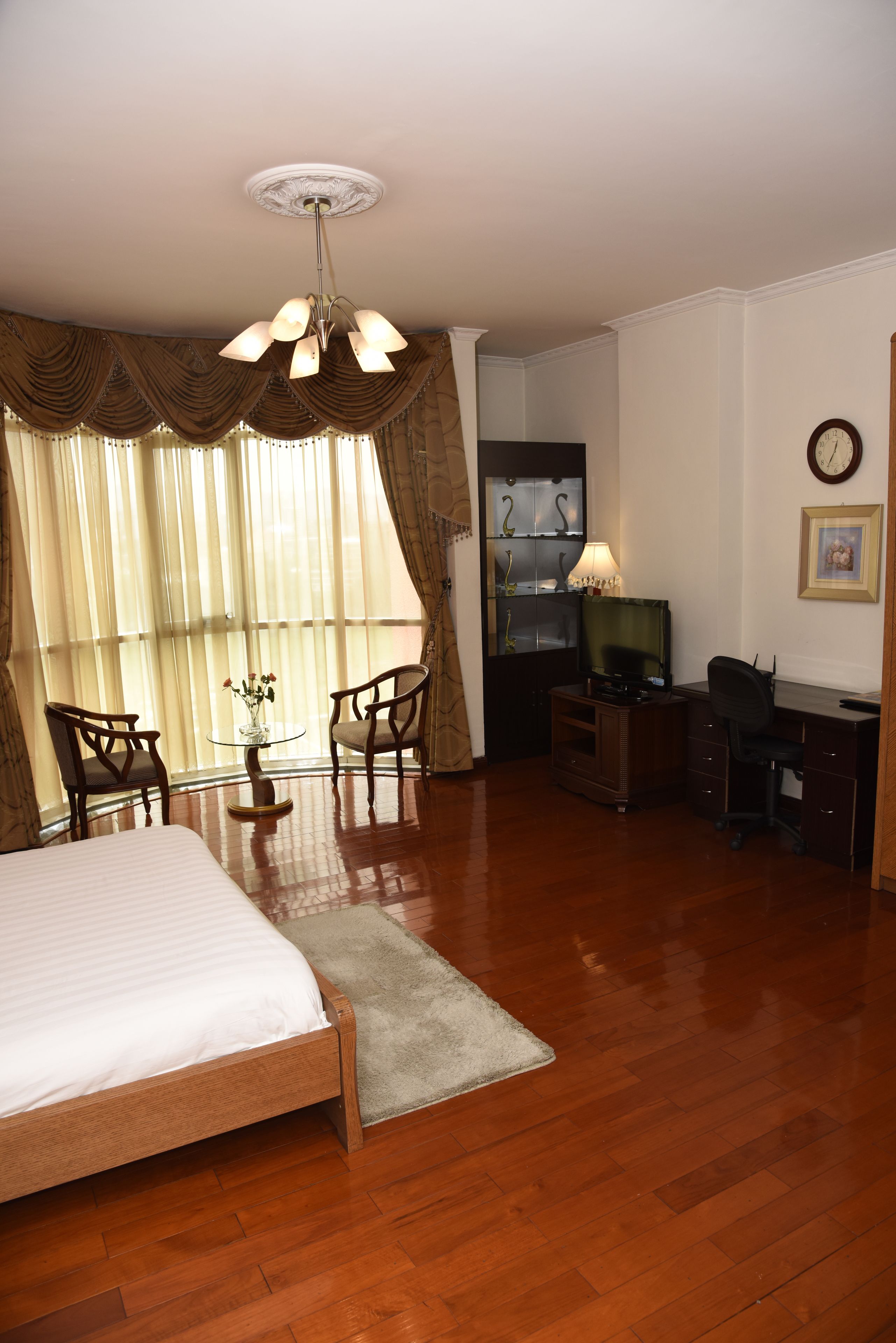 A hotel room with a bed, desk, chairs, a television, and a clock on the wall.