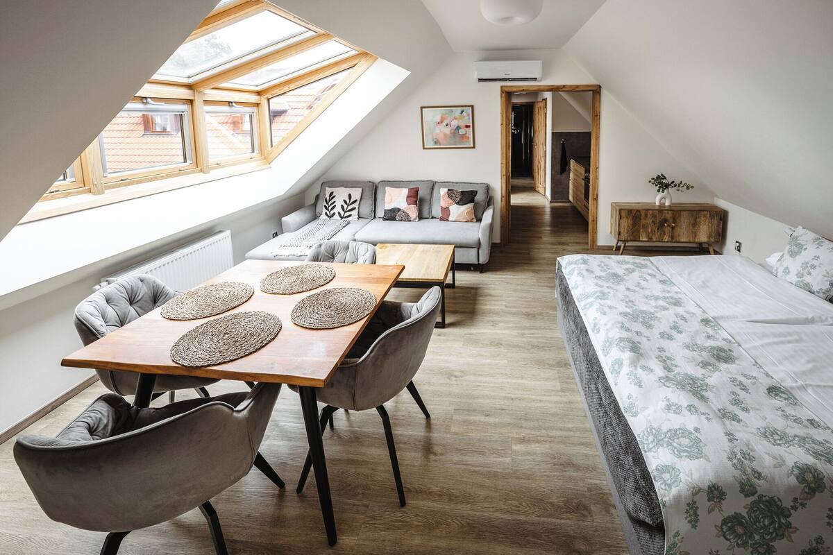 A cozy loft bedroom with a skylight, a sofa, a dining table with chairs, and a bed with floral bedding.