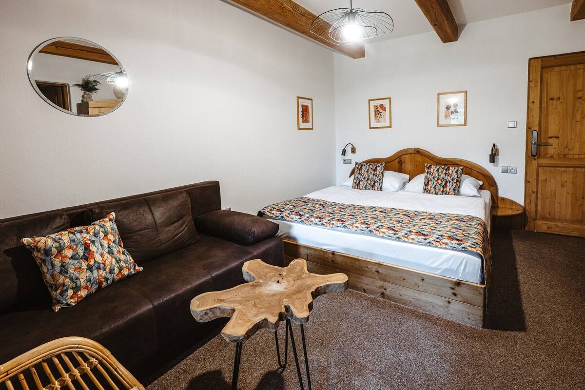 A bedroom with a wooden bed, a brown leather sofa, a round mirror, and a wooden coffee table.
