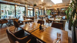 A restaurant with wooden tables and chairs, large windows, and hanging light fixtures. - Hotel Frýdl (Prague)