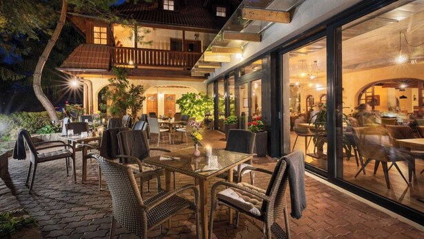 An outdoor dining area with wicker furniture and glass tables, overlooking a building with a balcony and large windows. - Hotel Frýdl (Prague)