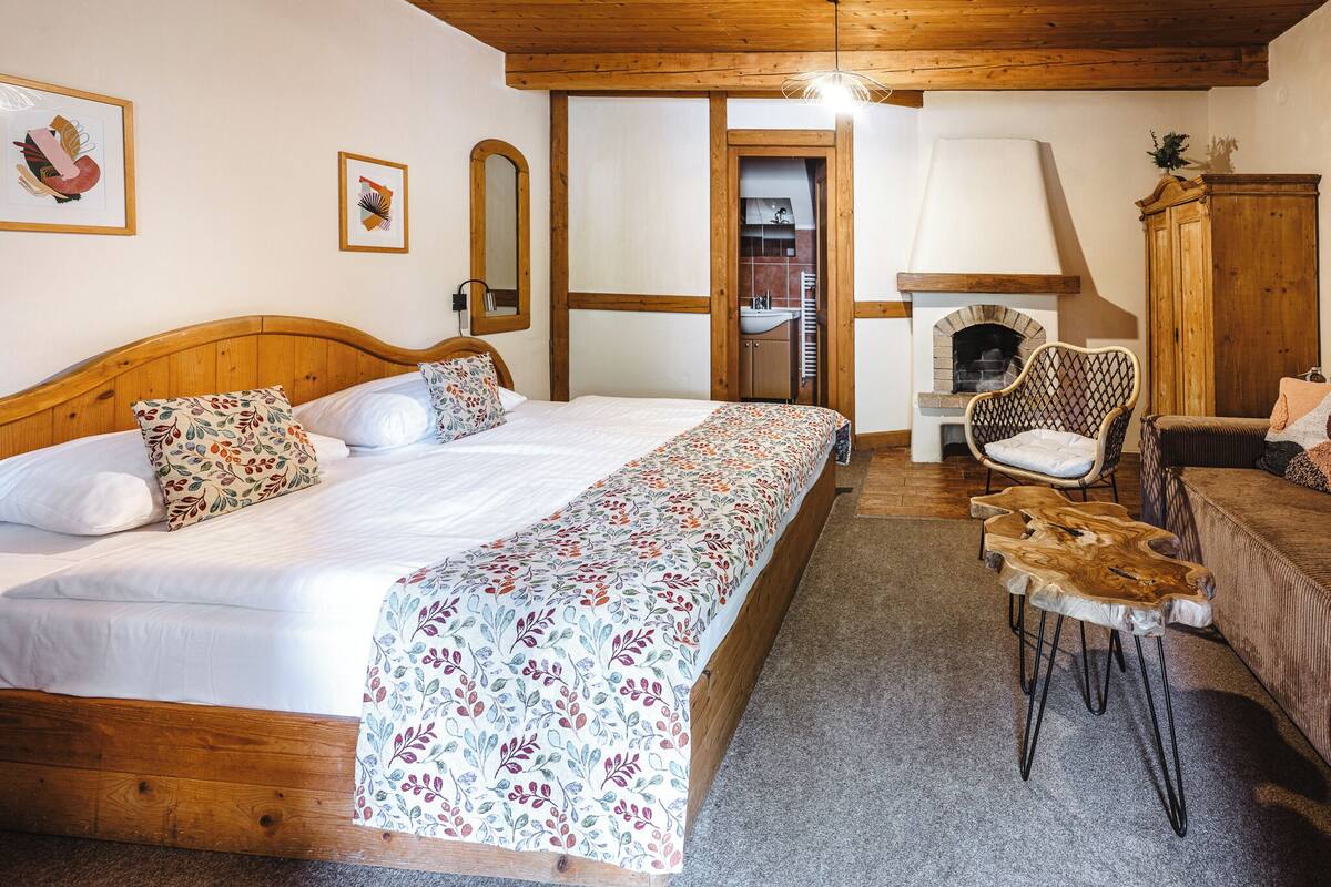 A bedroom with a wooden bed, a sofa, a chair, a fireplace, and a small bathroom visible through an open door.