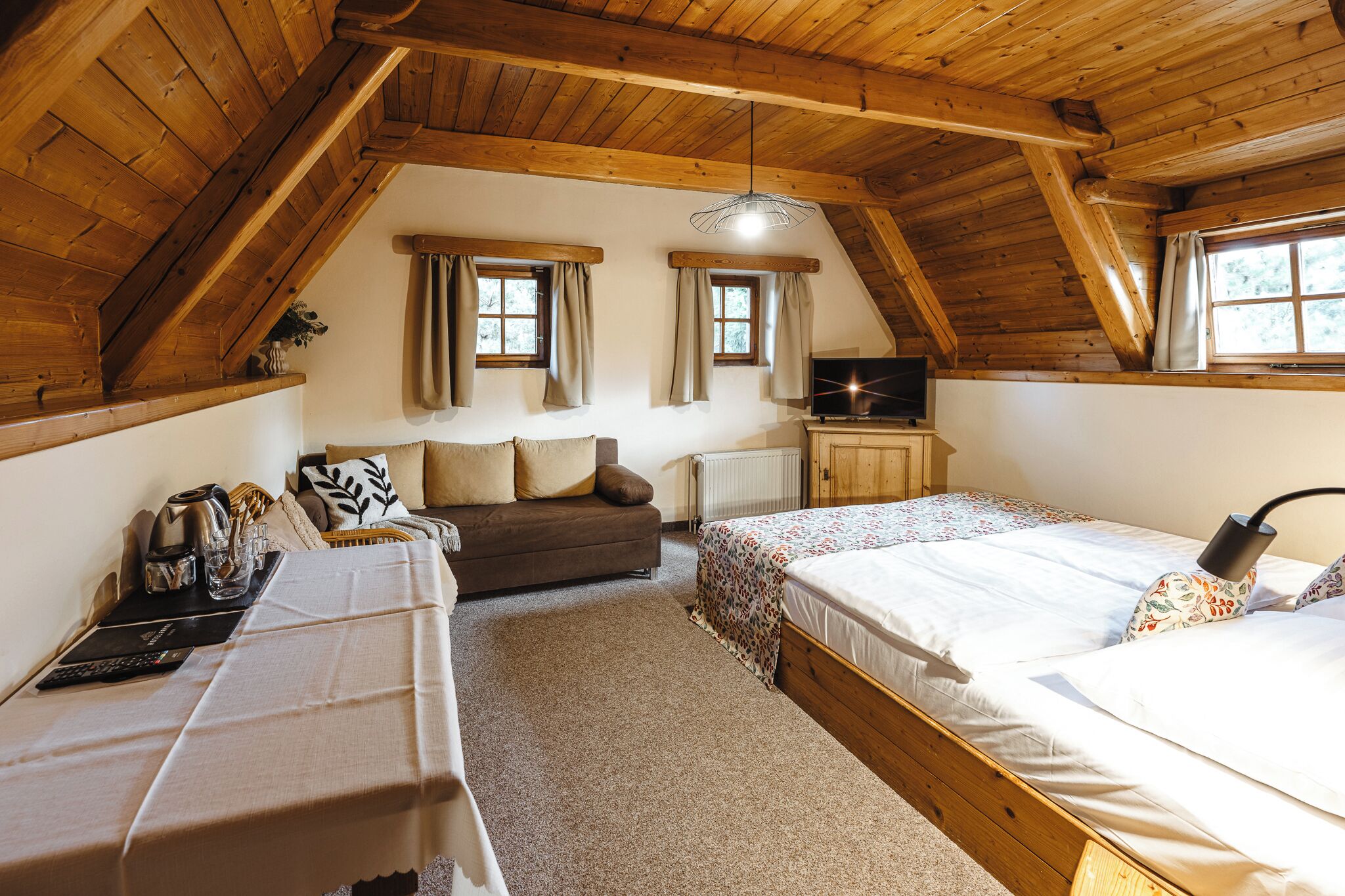 Un dormitorio acogedor en el ático, con techo de madera inclinado, dos camas, un sofá y un televisor.