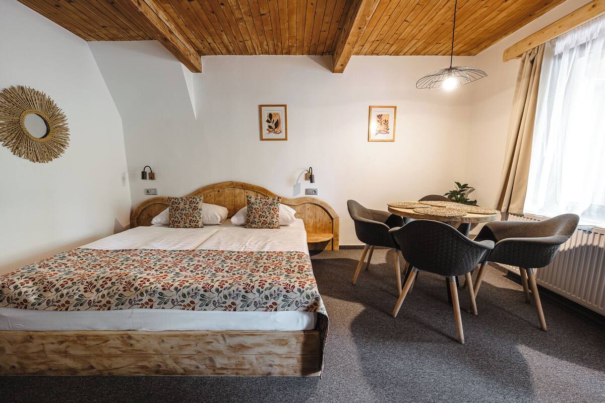 A bedroom with a wooden bed, a small table, two chairs, and a window with curtains.