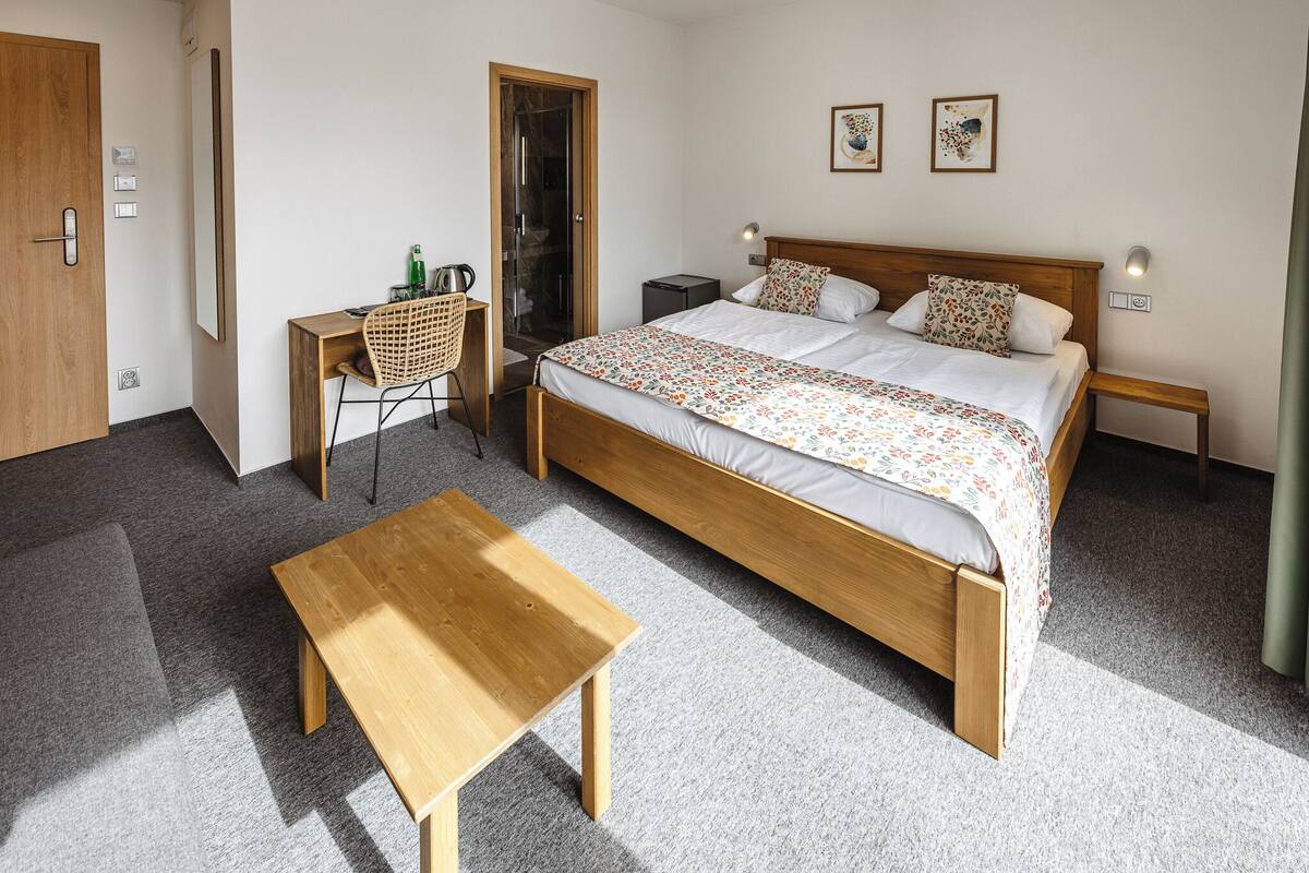 A bedroom with a wooden bed, a wooden desk, a chair, a bedside table, and a small table.