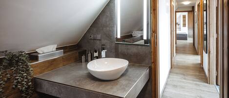 Un baño moderno con un lavamanos de pedestal grande, un espejo y un mueble de tocador de madera.
