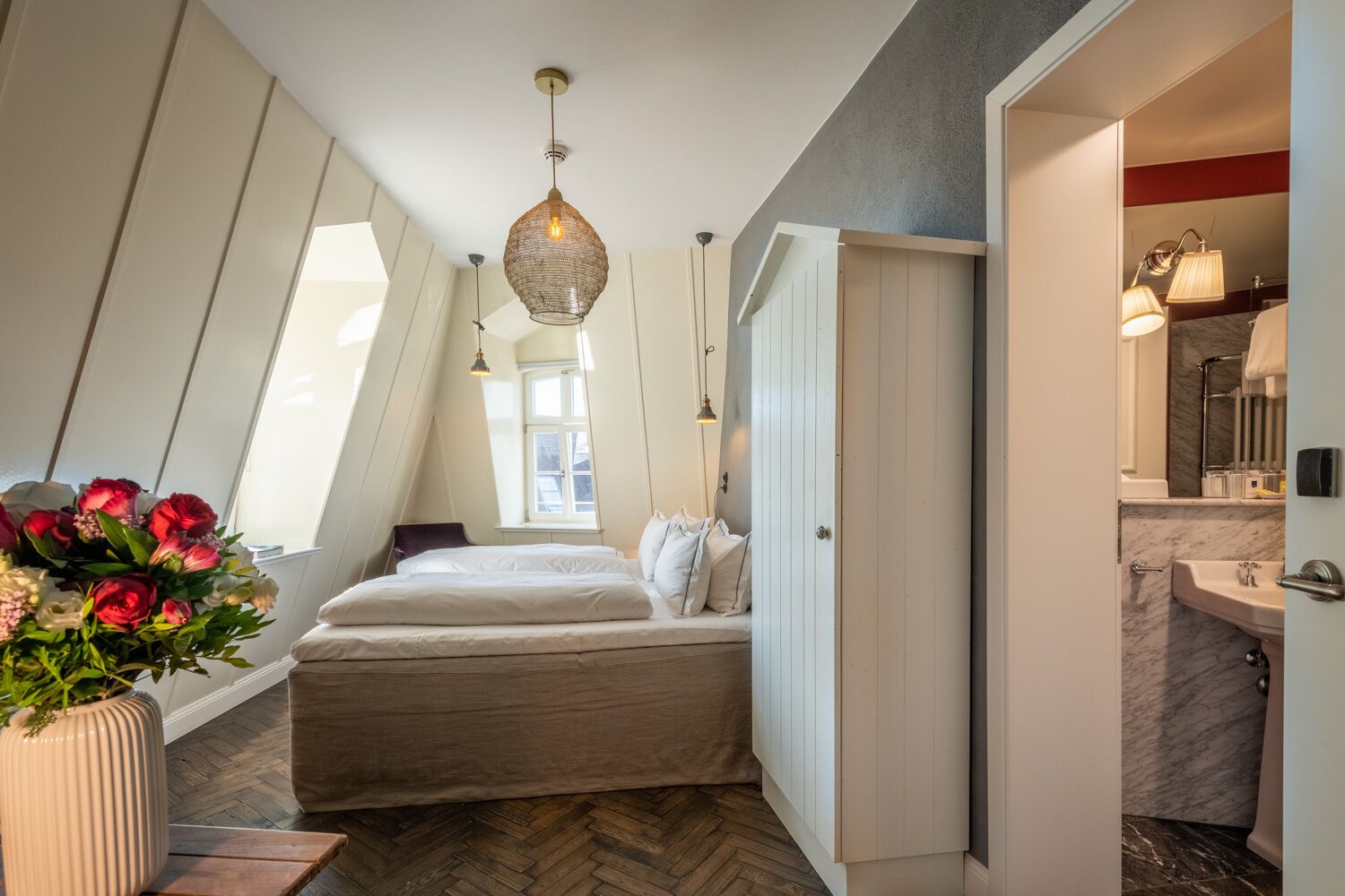 Un dormitorio con una cama, una lámpara colgante, un ventanal y vistas al baño.