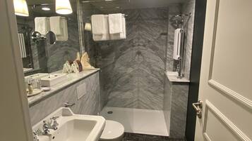 Un baño moderno con piso de mármol, un lavamanos, un inodoro, una ducha y un espejo con iluminación.