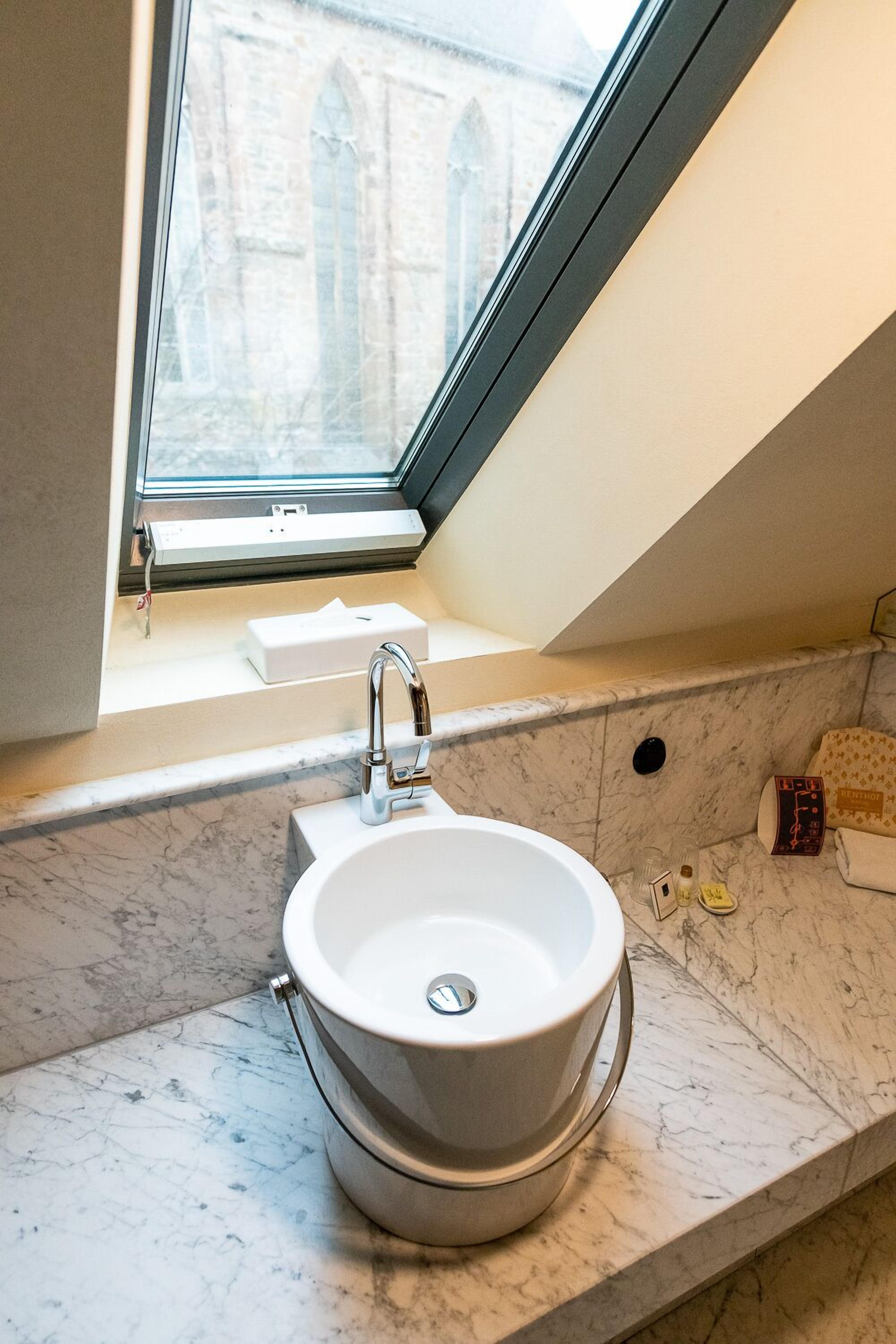 Une salle de bain avec un lavabo blanc, une fenêtre et une vue sur un bâtiment à l’extérieur.